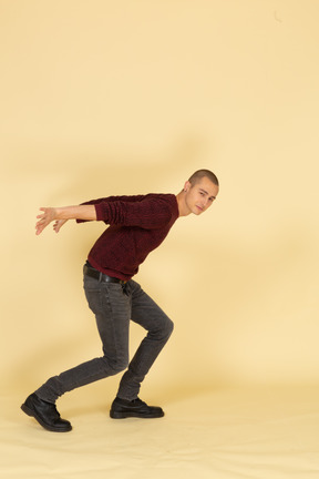 Side view of a young man in red pullover standing while taking hands behind