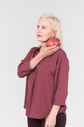 A nice-looking middle-aged blonde woman in a burgundy shirt and a pomegranate in her hand