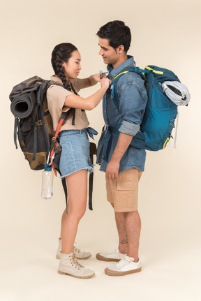 Riendo joven pareja interracial de pie cerca uno del otro con mochilas