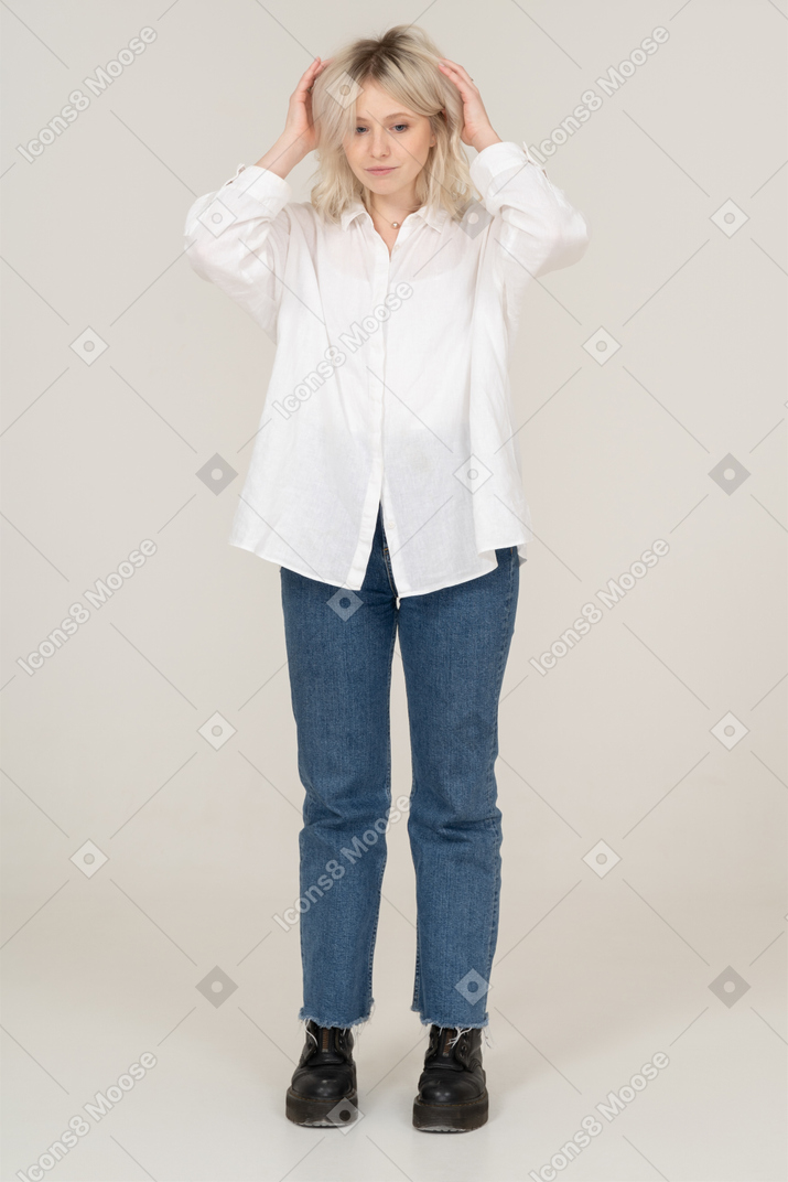 Vista frontal de una mujer rubia levantando las manos y tocando el cabello mientras mira hacia abajo