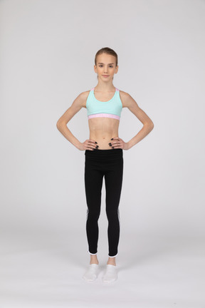 一个十几岁的女孩，将手放在臀部上的运动服的前视图