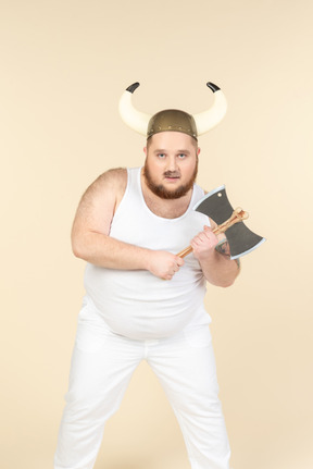 Un hombre de talla grande de color blanco con un casco con cuernos en la cabeza, sosteniendo un hacha de doble hoja