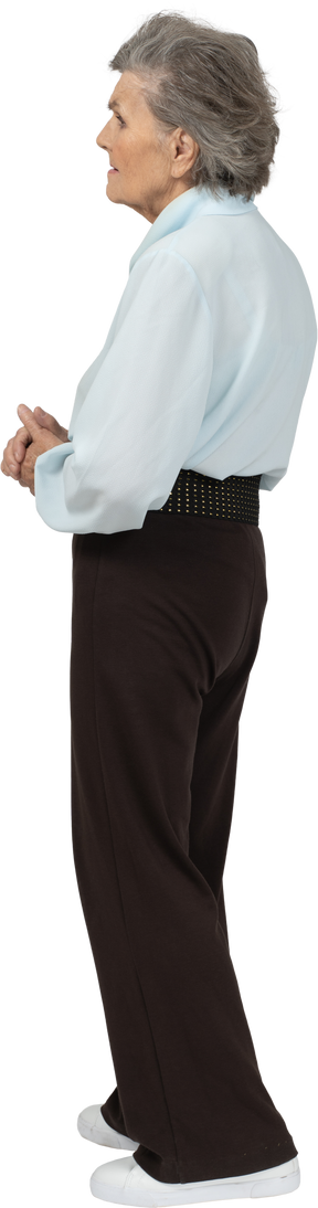 Vista lateral de una mujer vieja seria vestida con blusa y pantalones tomados de la mano juntos