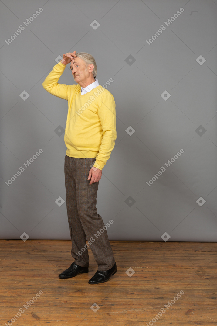 Vue de trois quarts d'un vieil homme confus touchant la tête et portant un pull jaune