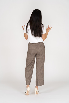 Vista posteriore di una giovane donna chiedendo in calzoni e t-shirt alzando le mani