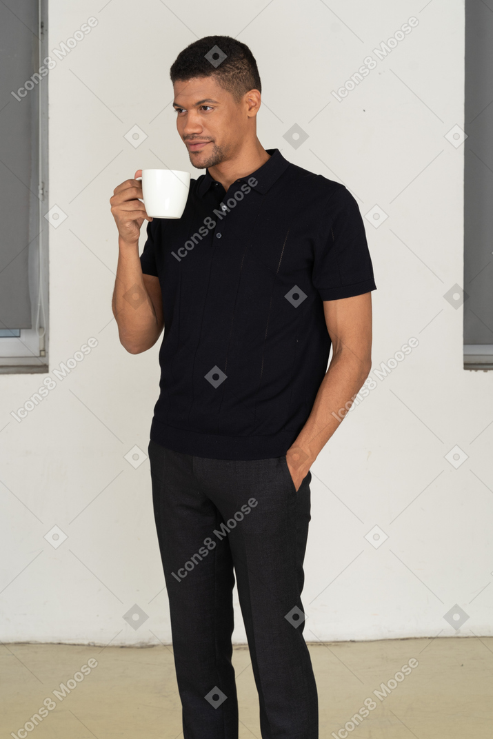 Standing half sideways young man in black pants and t-shirt holding cup