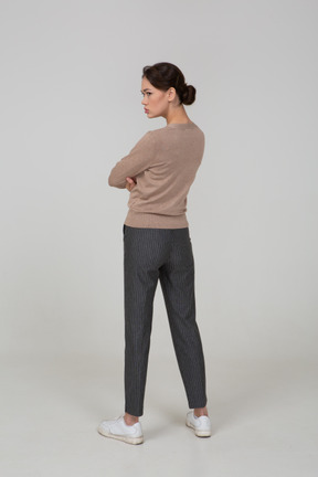 Three-quarter back view of an offended young lady in pullover and pants crossing hands
