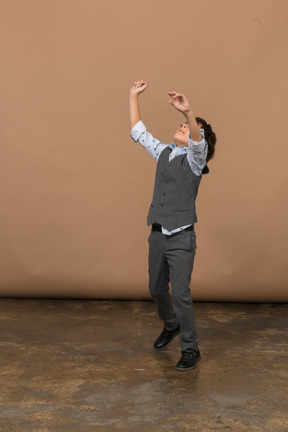 一个穿着西装的男孩举起双臂站立的侧视图