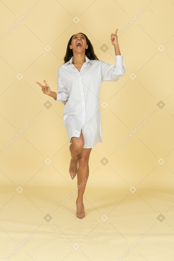 Front view of a screaming dark-skinned young female in white dress raising hands