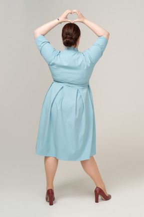 Вид сзади женщины в синем платье, показывающей жест сердца