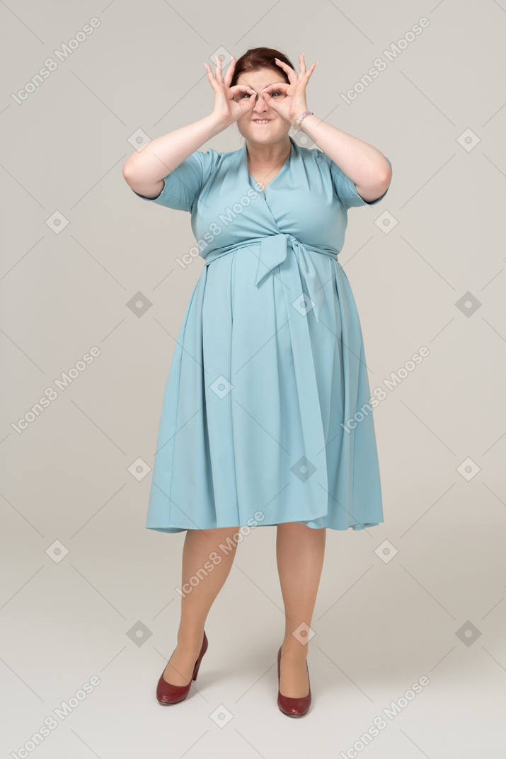 Vista frontal de una mujer en vestido azul mirando a través de binoculares imaginarios