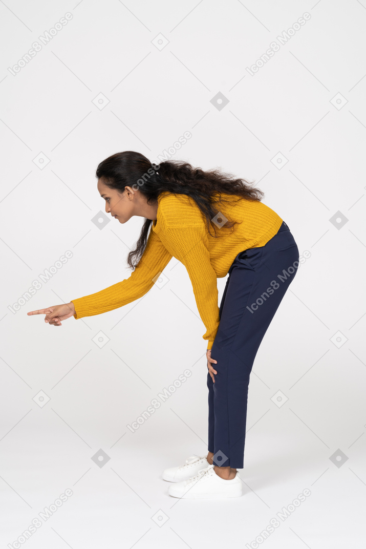 Side view of a girl in casual clothes bending down and pointing with finger
