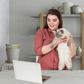 A woman holding a cat in front of a laptop