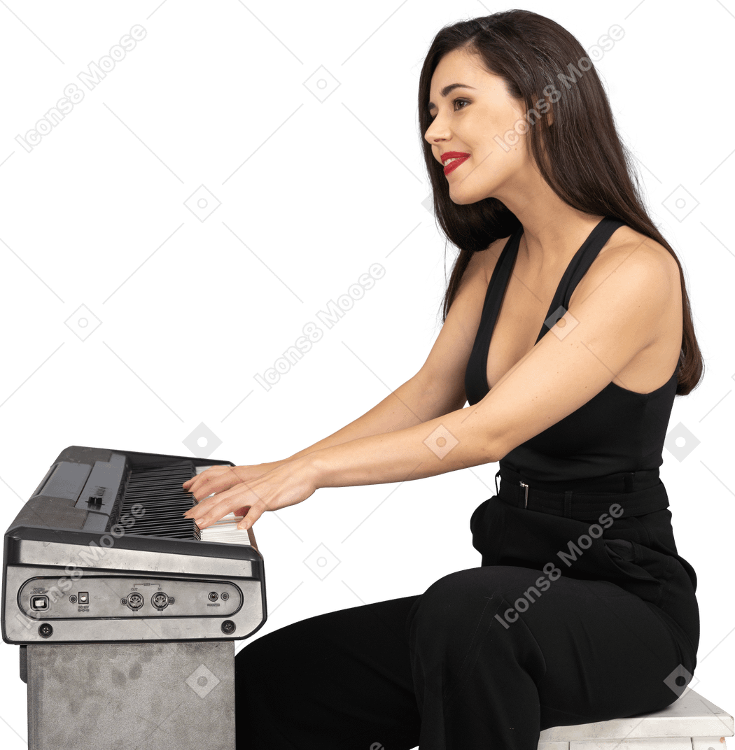 Vue latérale d'une jeune femme assise souriante en costume noir tout en jouant du piano