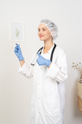 Vista de três quartos de uma jovem médica sorridente com um estetoscópio segurando o termômetro e mostrando o polegar
