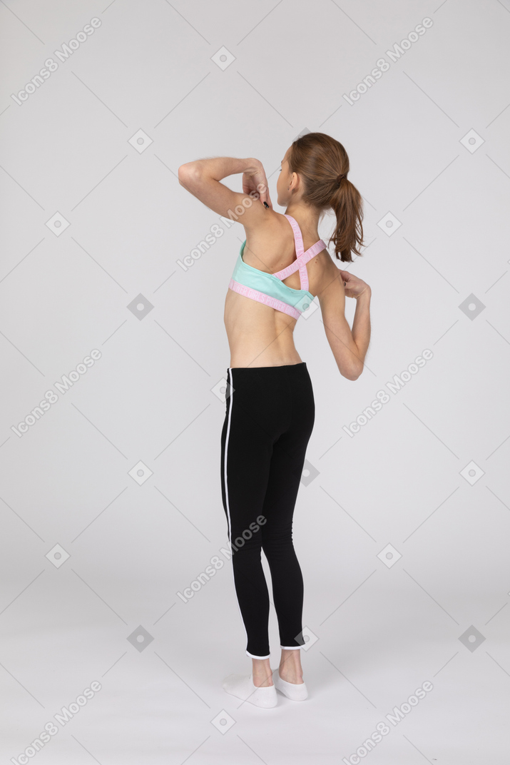 Три четверти сзади девушки-подростка в спортивной одежде, касающейся ее плеч и наклоненной вправо