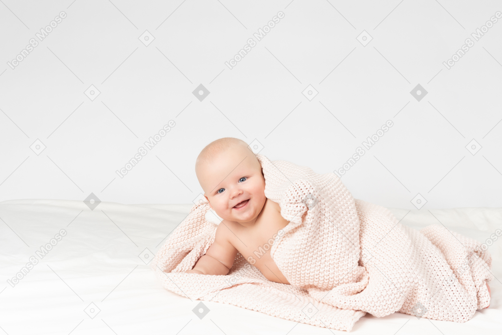 Smiling baby boy covered in beige knitted blanket