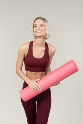 Sonriente mujer joven en ropa deportiva con estera de yoga