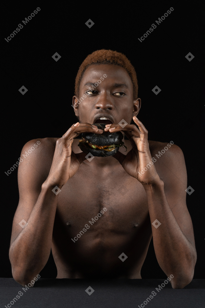 Vue de face d'un jeune homme afro mordant un hamburger