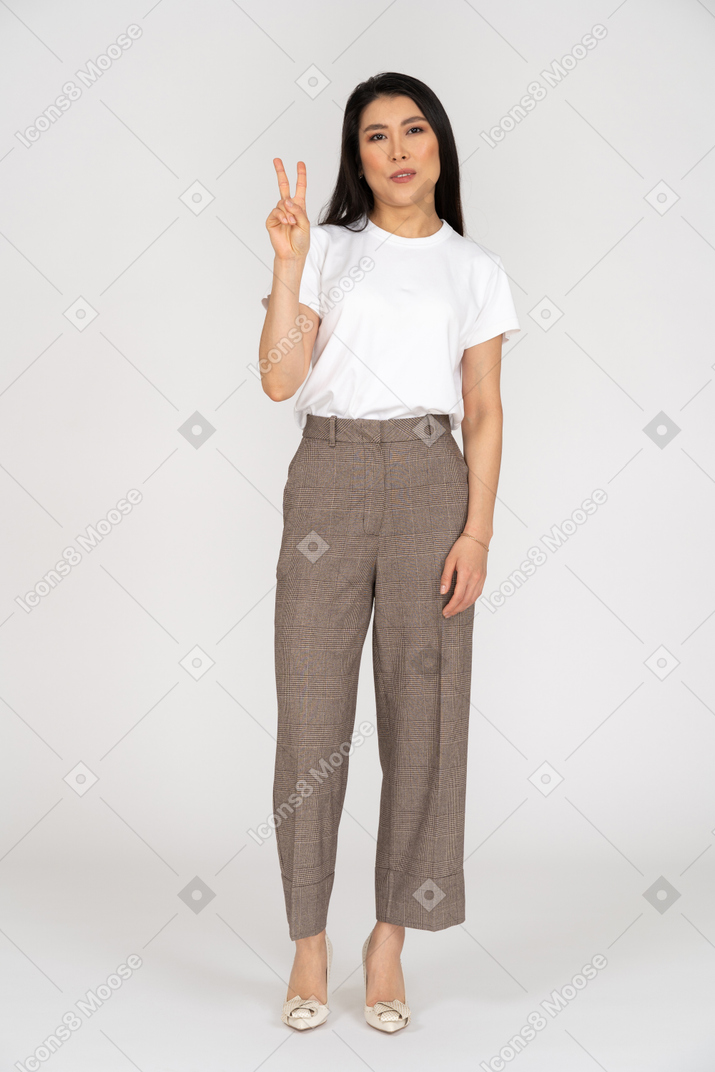 Vista frontale di una giovane donna in calzoni che mostra il segno di pace