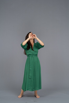 手を上げながらフルートを演奏する緑のドレスを着た若い女性の正面図