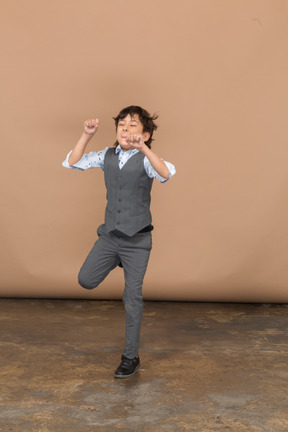 一个穿着西装的可爱男孩举起双臂跳跃的正面图