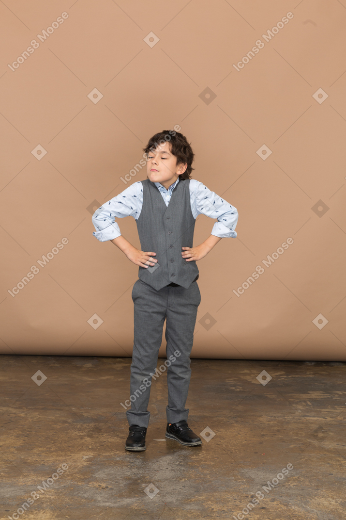 Vista frontal de un niño con traje gris posando con las manos en las caderas