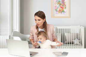 A woman holding a baby in front of a laptop