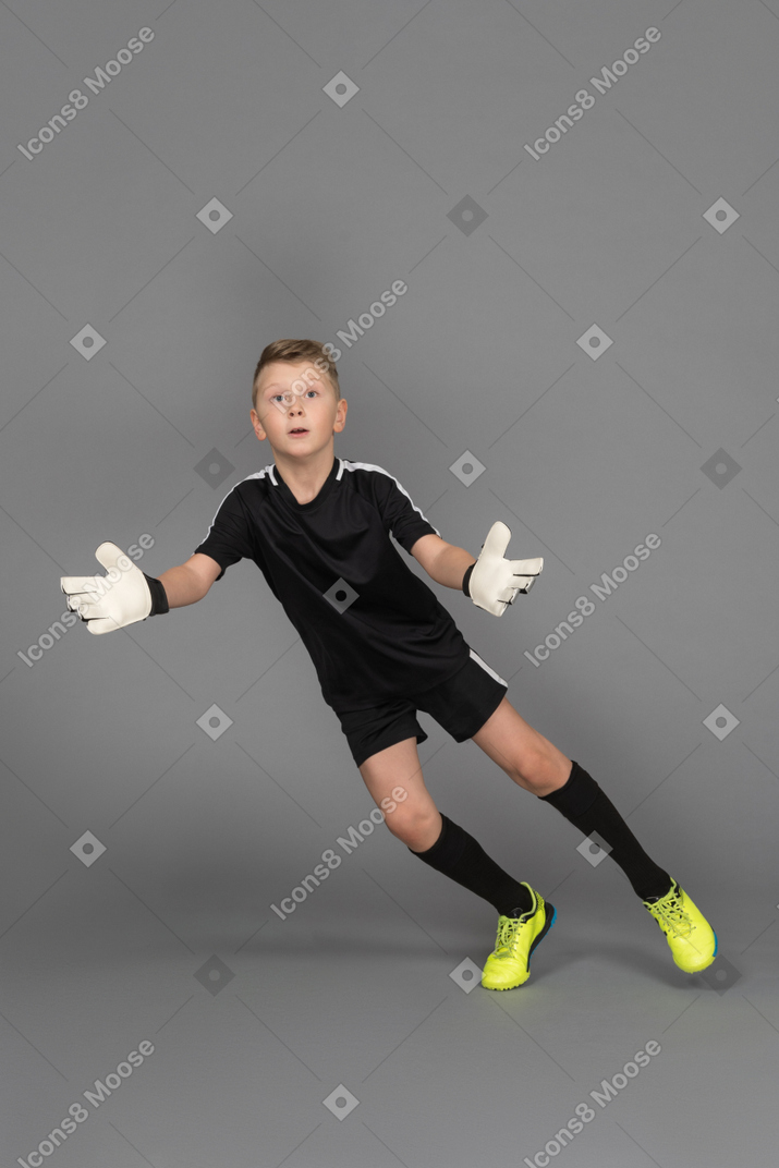 Front view of a kid boy goalkeeper jumping and outstretching hand