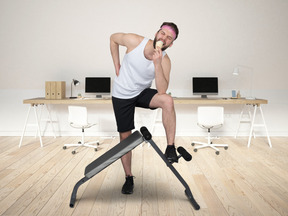 A man standing next to a fitness equipment in the office and eating ice cream