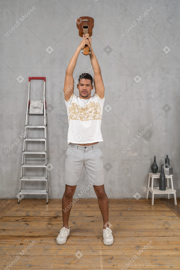 Front view of a man lifting an ukulele above his head