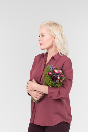 A nice-looking middle-aged blonde woman in a burgundy shirt and with a simple bouquet of flowers in her hands