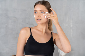 Mujer joven quitando la crema facial con una almohadilla de algodón