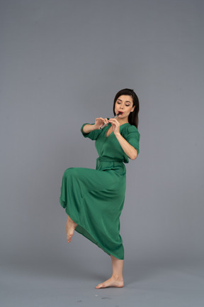 Vista lateral de uma jovem dançando com vestido verde tocando flauta
