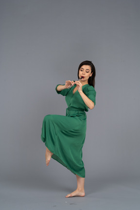 Side view of a dancing young lady in green dress playing flute