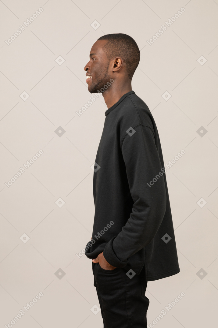 Side view of a smiling young man keeping hands in pockets