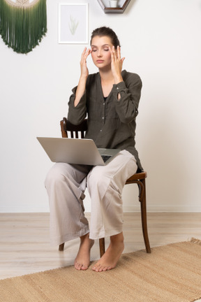 ノートパソコンで椅子に座っている頭痛のある忙しい若い女性の4分の3のビュー