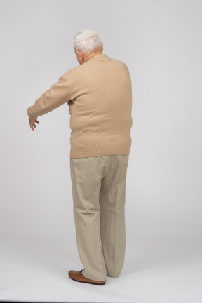 Rear view of an old man in casual clothes standing with extended arm