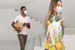 A man and a woman in face masks carrying groceries bags