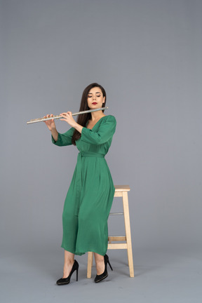 Figura intera di una giovane donna in abito verde seduta su una sedia mentre suona il clarinetto