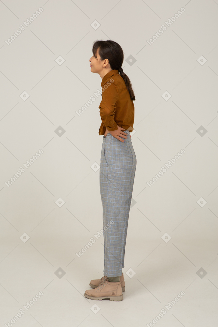 Vista laterale di una giovane donna asiatica in calzoni e camicetta che mette le mani sui fianchi