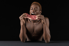 Front view of a young afro man biting a slice of meat