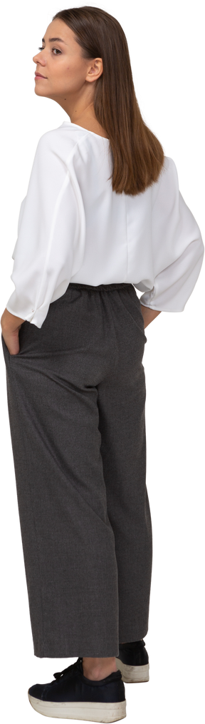 Vista posteriore di tre quarti di una giovane donna in abiti da ufficio che mette le mani in tasca e guarda da parte