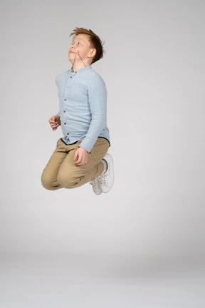 A boy in a blue shirt jumping with bent knees