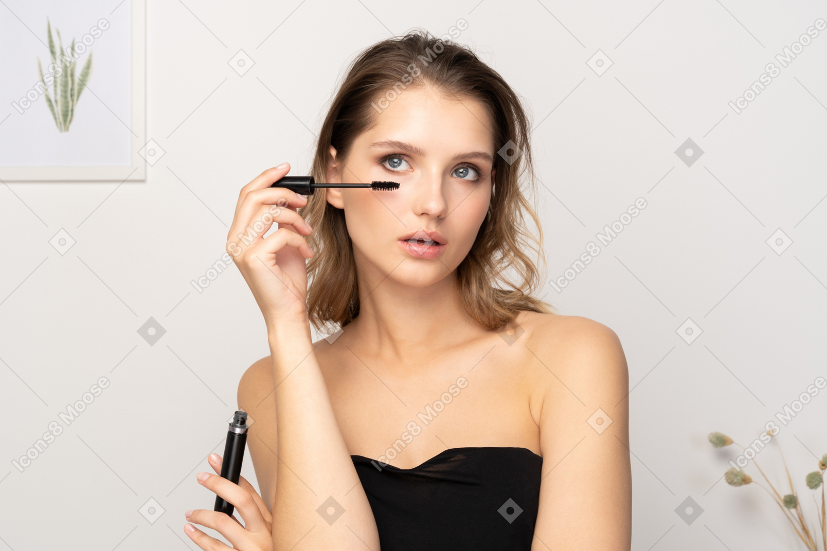 Front view of a young woman wearing black top applying mascara