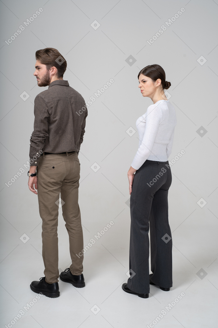 Three-quarter back view of a displeased young couple in office clothing knitting brows