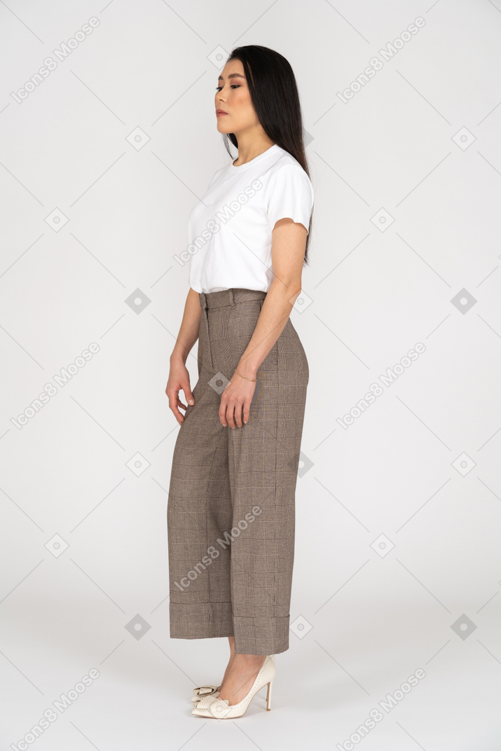 Three-quarter view of a young woman in breeches standing still while looking down