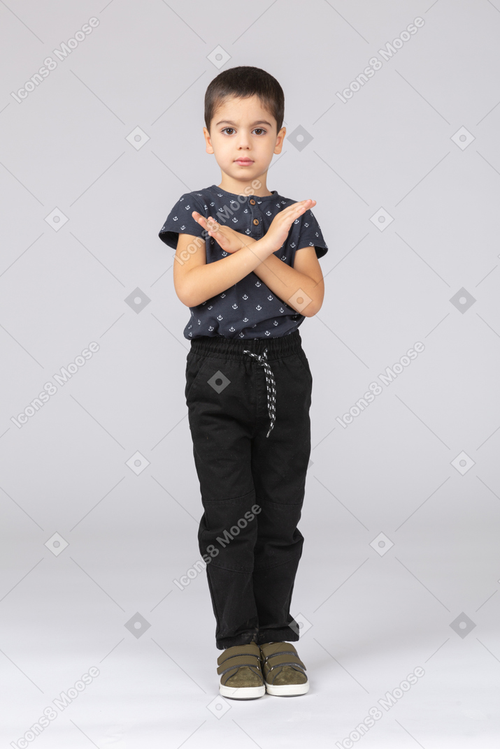 Cute boy in casual clothes looking at camera and showing stop gesture
