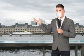 Reporter in a mask gesturing towards a city background
