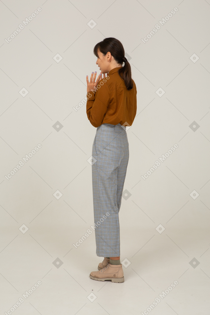 Three-quarter back view of a young asian female in breeches and blouse raising hands